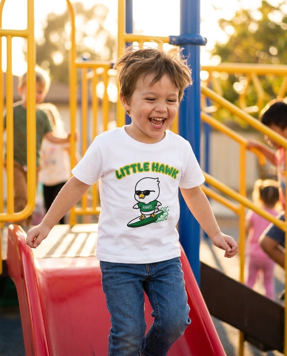 A preschooler laughing on the playground in the Little Hawk youth tee