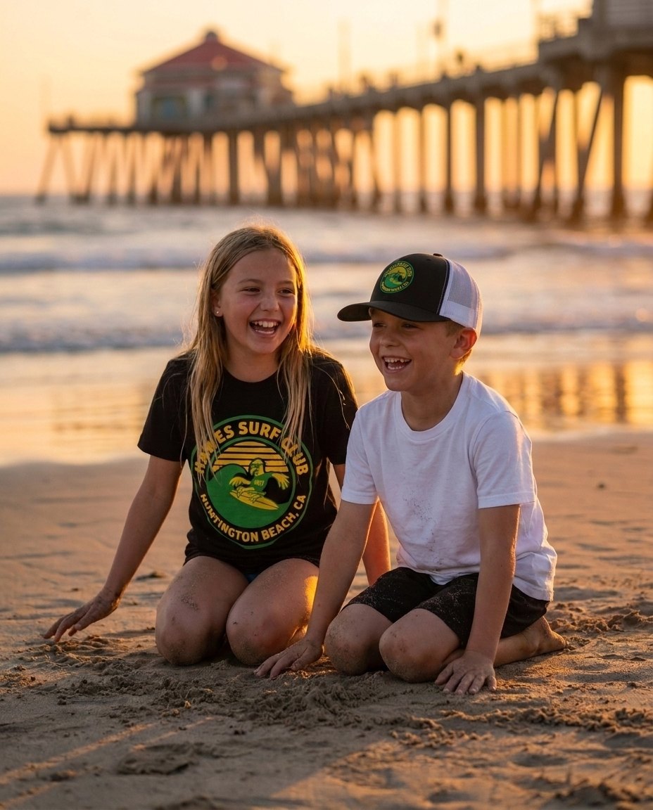 Two kids on the sand by the Huntington Beach pier in the Hawes Surf Club tee and embroidered trucker hat